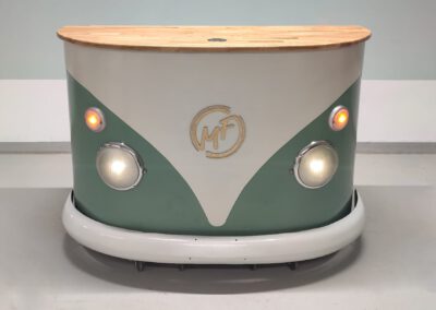 Messestand oder Tresen zum Mieten aus Holz mit türkisfarbener Bulli Front und Logo von Moment Fabrik. Ideal für Öffentliche Veranstaltungen, Messen oder Private Feiern. Original Stoßstange vom VW T1 Bus.